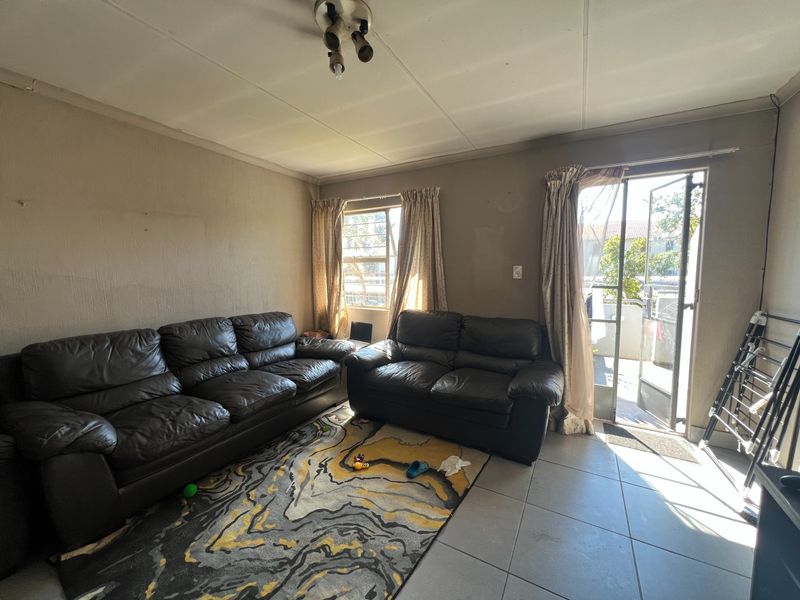A living room featuring tiled flooring and direct access to an outdoor area through a sliding glass door with a security gate.