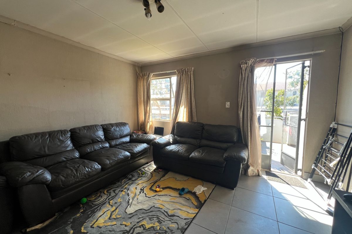 A living room featuring tiled flooring and direct access to an outdoor area through a sliding glass door with a security gate.