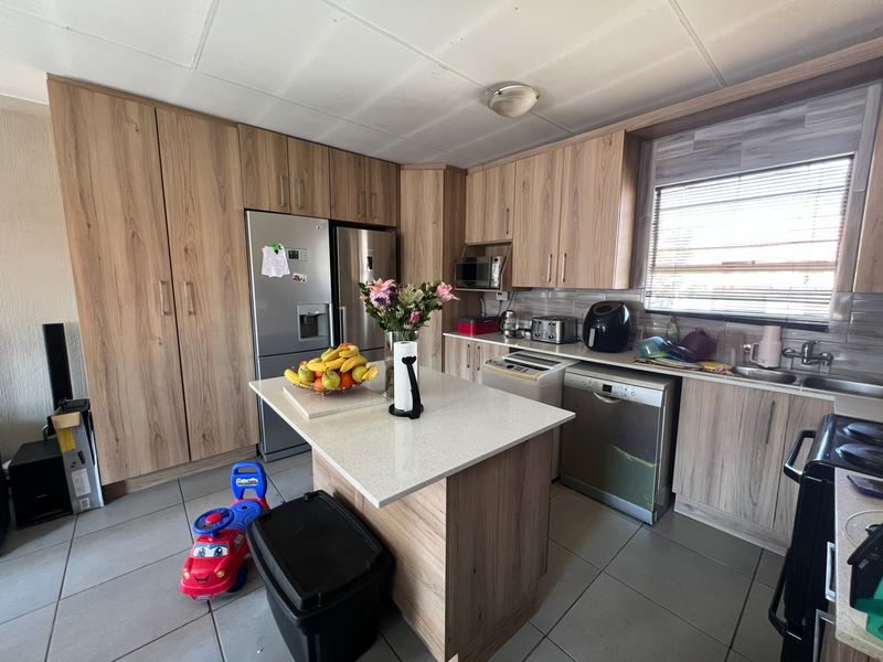 A functional kitchen featuring light wood-grain cabinetry, a central island with stone countertops, tiled flooring, and ample storage space.