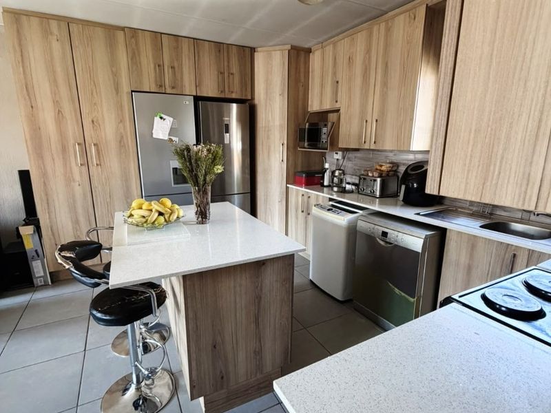 Modern kitchen featuring light wood-grain cabinetry, stone countertops, a central island, and tiled flooring, providing a functional and contemporary cooking space.