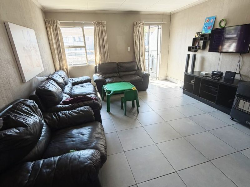 Spacious living room featuring large floor tiles, neutral wall finishes, and direct access to a balcony through a sliding glass door.