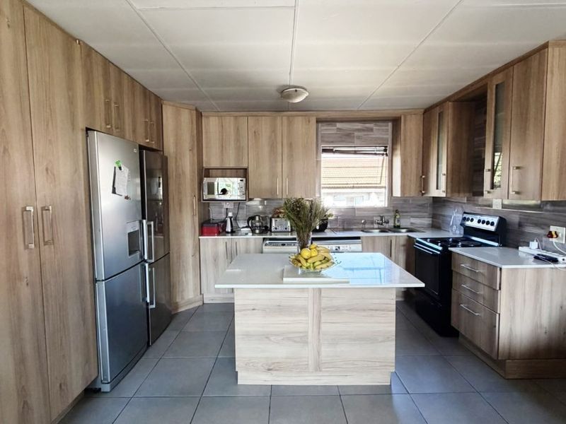 A well-maintained kitchen featuring light wood-finish cabinetry, a central island, stone countertops, and large format floor tiles.