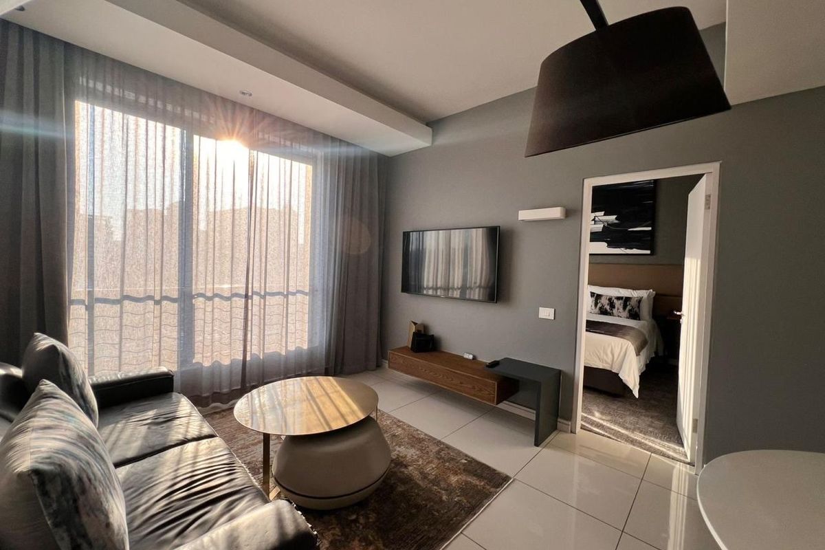 Modern living room featuring large floor-to-ceiling windows, tiled flooring, and a wall-mounted media console, with direct access to an adjacent bedroom.