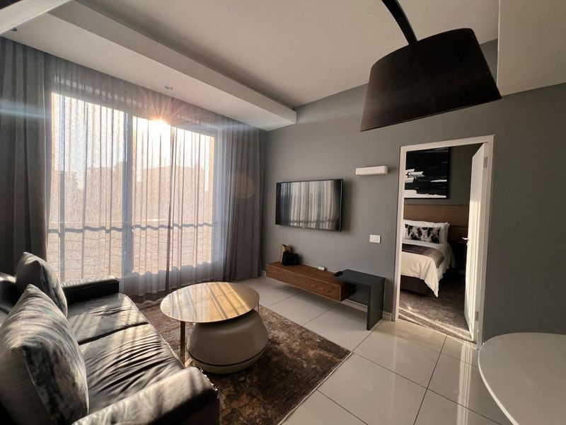 Modern living room featuring large floor-to-ceiling windows, tiled flooring, and a wall-mounted media console, with direct access to an adjacent bedroom.