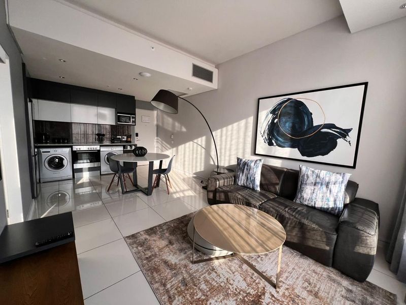 Modern open-plan apartment living area featuring a sleek kitchen with integrated appliances, tiled flooring, and contemporary finishes throughout.