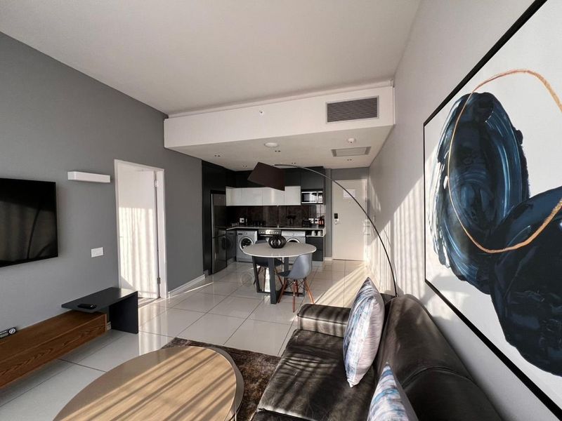 Modern open-plan living area featuring a sleek kitchen with integrated appliances, tiled flooring, and ducted air conditioning, creating a functional and contemporary space.