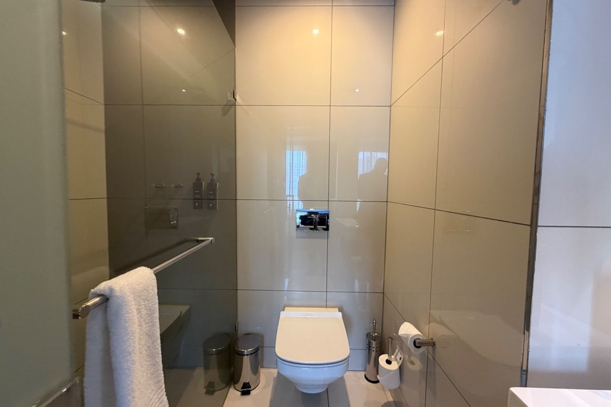 Modern bathroom featuring a wall-mounted toilet, glass shower screen with rain shower head, and neutral floor-to-ceiling tiling.