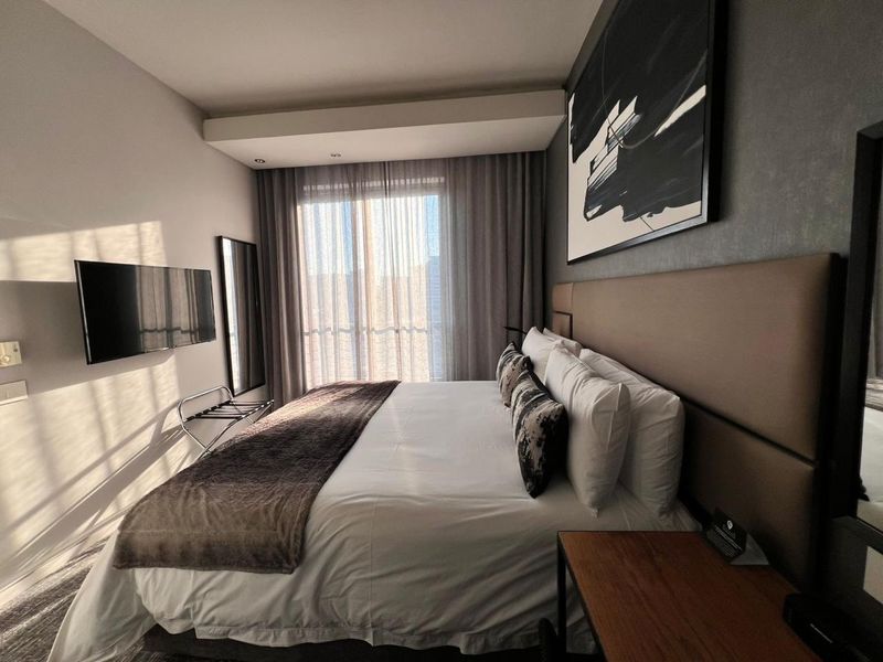 Modern bedroom featuring a large upholstered headboard, recessed ceiling lighting, and floor-to-ceiling curtains with access to natural light.