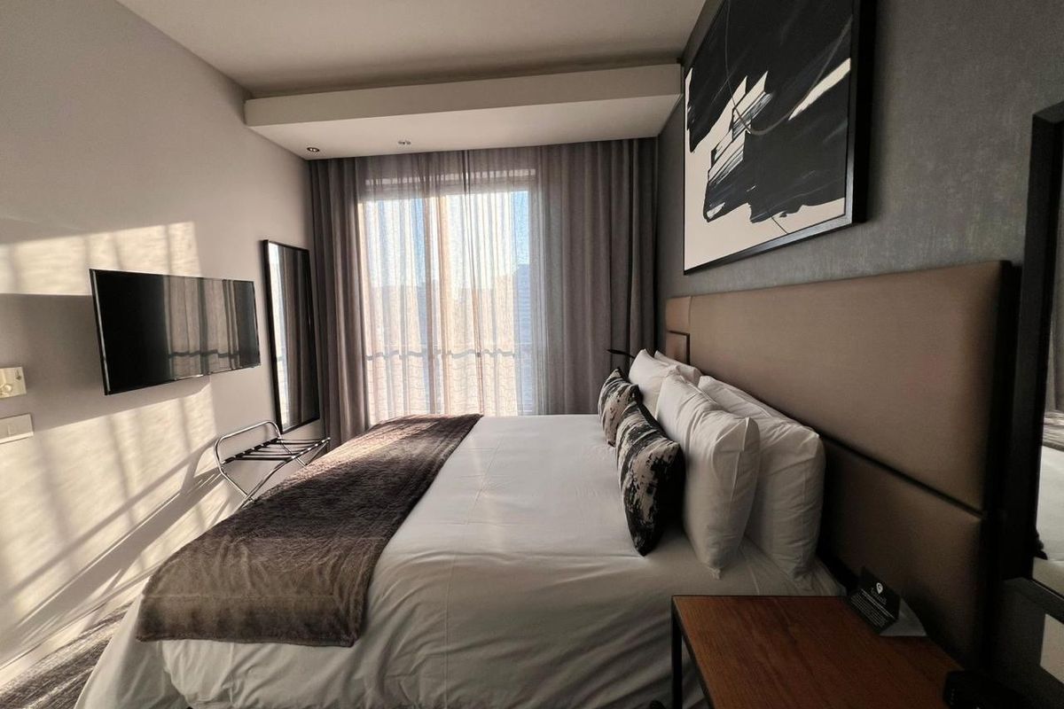 Modern bedroom featuring a large upholstered headboard, recessed ceiling lighting, and floor-to-ceiling curtains with access to natural light.