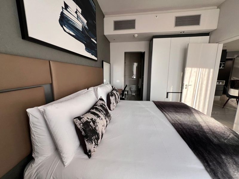 Modern bedroom featuring a built-in wardrobe, integrated ducted air conditioning, and an en-suite bathroom, finished with a contemporary upholstered headboard.