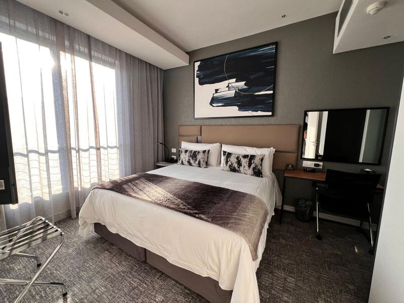 A well-maintained bedroom featuring a built-in headboard, recessed ceiling lighting, and large windows with floor-to-ceiling curtains.