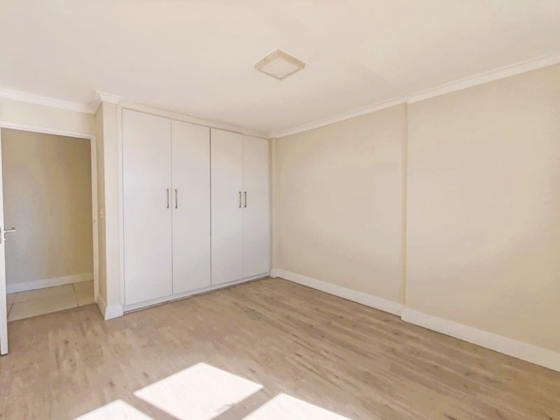 A bright, empty bedroom featuring neutral walls, light-toned laminate flooring, and ample built-in cupboard storage.