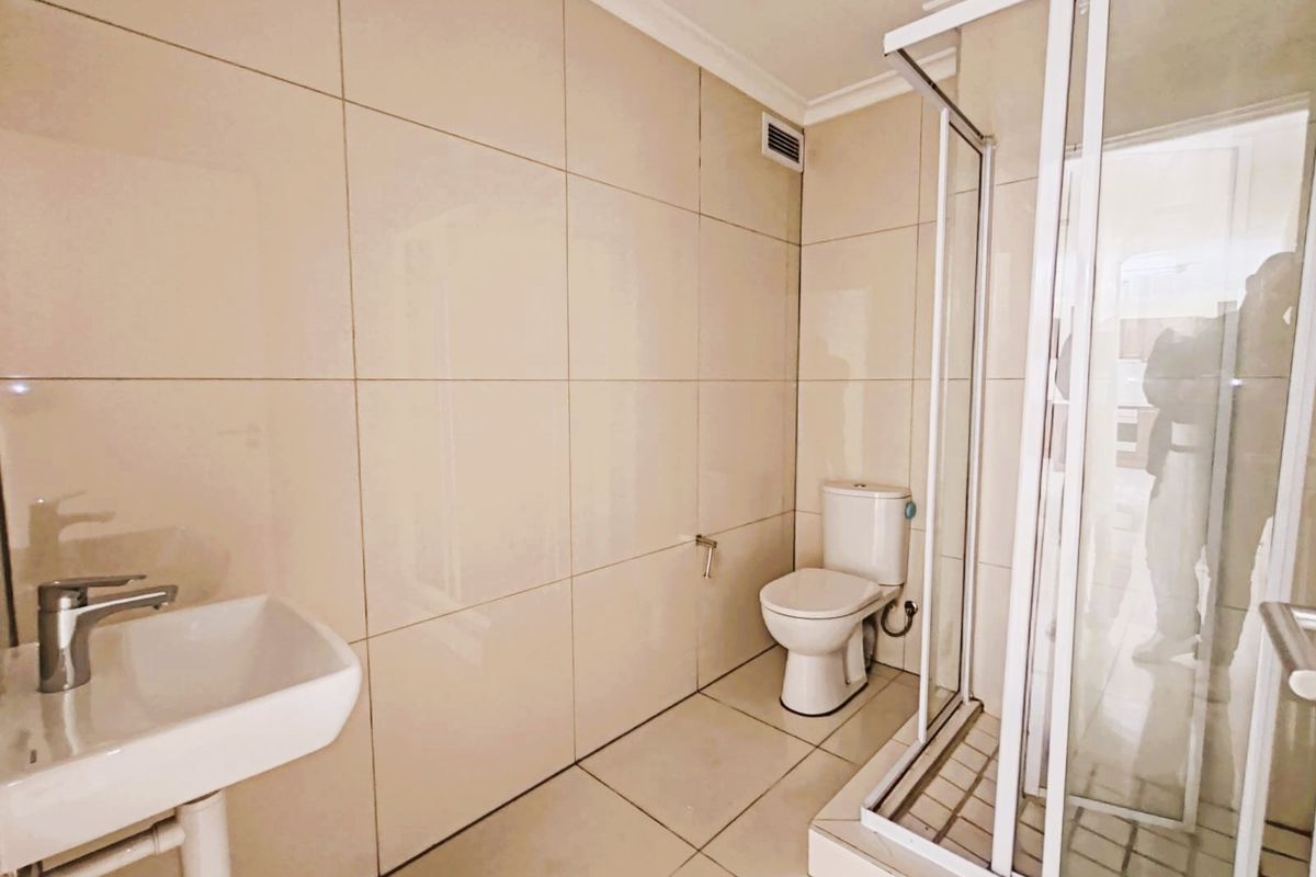 A clean, modern bathroom featuring neutral wall and floor tiles, a wall-mounted basin, a toilet, and a glass-enclosed shower unit.