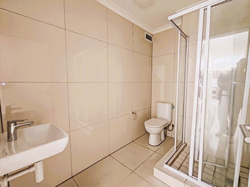 A clean, modern bathroom featuring neutral wall and floor tiles, a wall-mounted basin, a toilet, and a glass-enclosed shower unit.