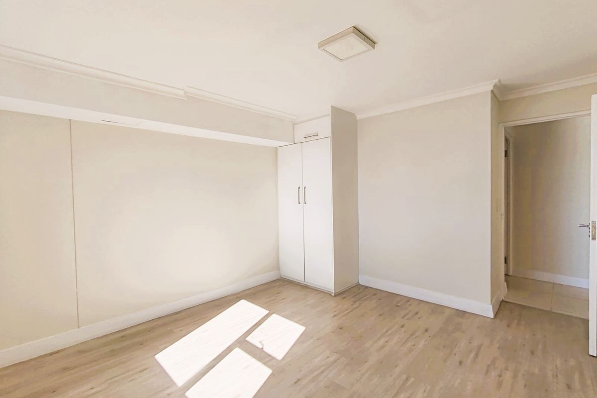 A bright, empty bedroom featuring light-toned laminate flooring, neutral walls, and a functional built-in cupboard with overhead storage.