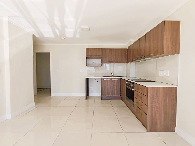A clean, modern kitchen featuring dark wood cabinetry, integrated appliances, light tiled flooring, and a neutral backsplash in an open-plan layout.