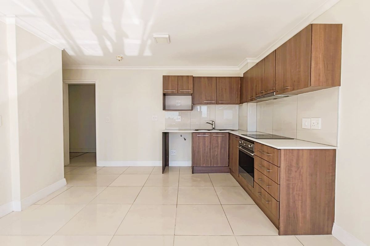 A clean, modern kitchen featuring dark wood cabinetry, integrated appliances, light tiled flooring, and a neutral backsplash in an open-plan layout.