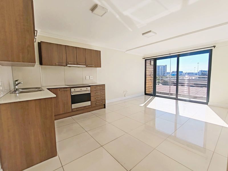 Modern open-plan kitchen and living area featuring tiled floors, built-in cabinetry, integrated appliances, and large sliding doors leading to a balcony with city views.