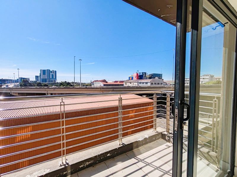 A balcony featuring a stainless steel balustrade and tiled flooring, offering an urban view of the surrounding city infrastructure.