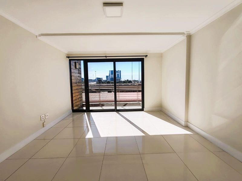 A bright, empty living room featuring neutral tiled flooring and a large sliding glass door leading to an outdoor balcony with city views.