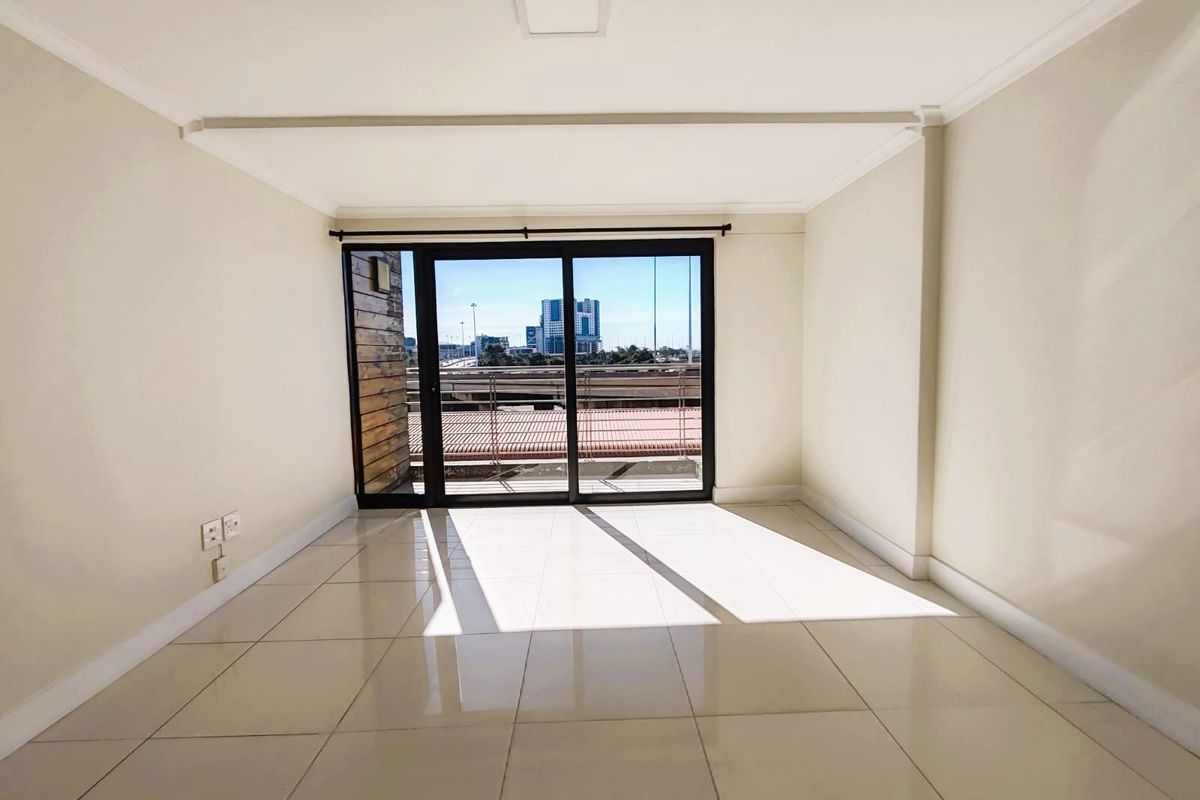 A bright, empty living room featuring neutral tiled flooring and a large sliding glass door leading to an outdoor balcony with city views.
