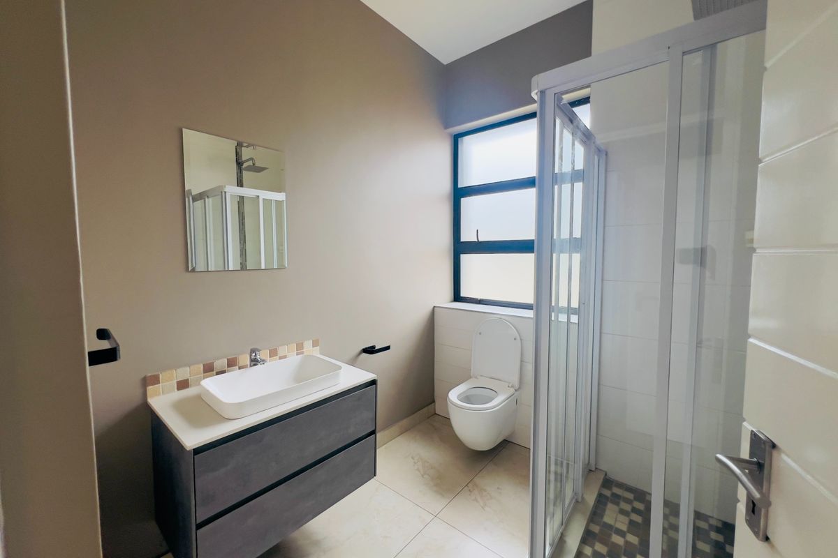 Modern bathroom featuring a wall-mounted toilet, vanity with vessel sink, and a glass-enclosed shower with a rain shower head.
