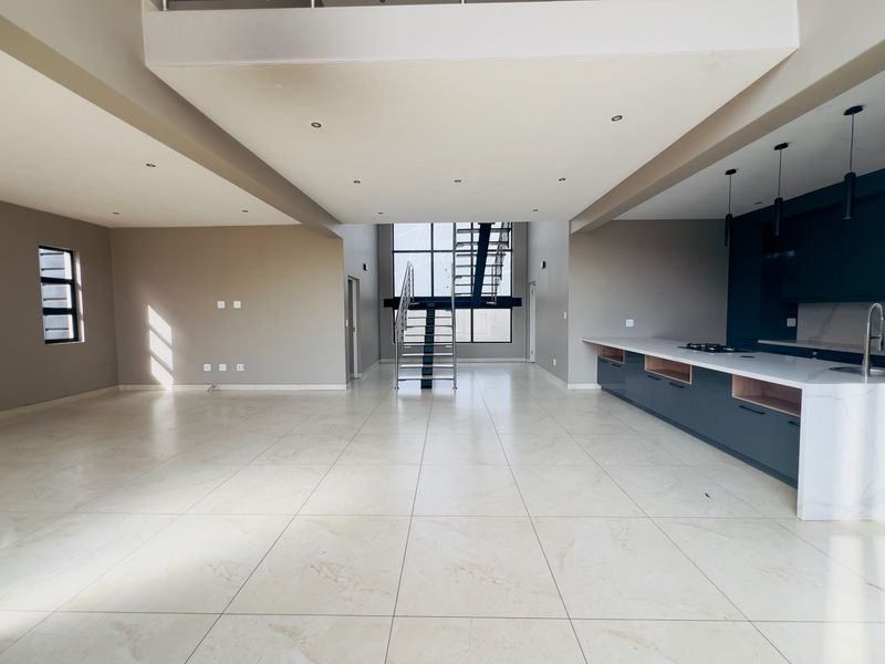 Spacious open-plan living and kitchen area featuring modern dark cabinetry, stone island, large porcelain tiles, and a striking double-volume staircase.