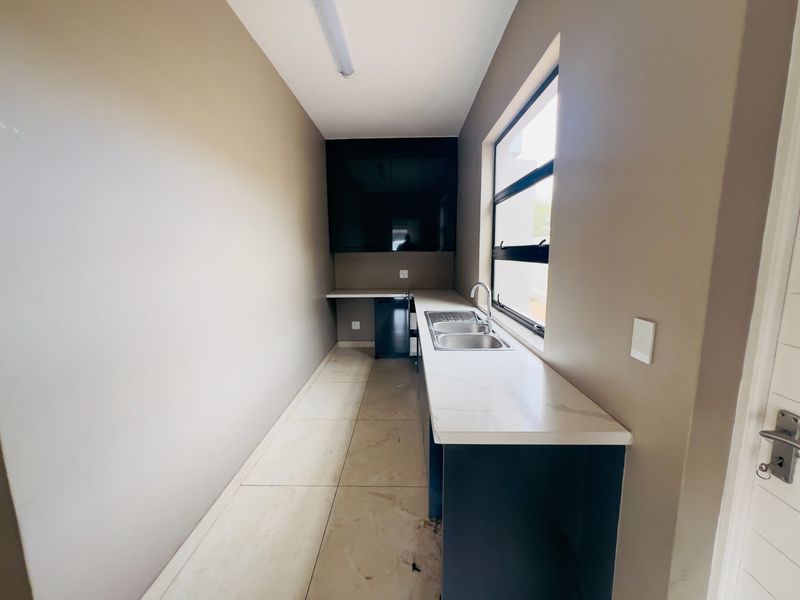 A clean, modern scullery featuring a double bowl sink, stone countertops, and ample built-in cabinetry, providing a functional and organized utility space.