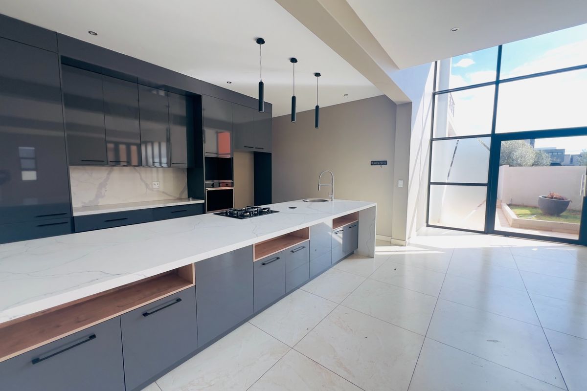 Modern kitchen featuring sleek grey cabinetry, quartz countertops, integrated appliances, and expansive floor-to-ceiling windows providing natural light and garden access.