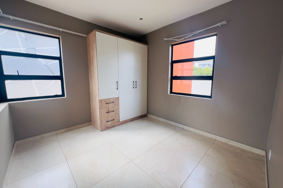 A bright, empty bedroom featuring neutral tiled flooring, built-in cabinetry, and modern aluminium-framed windows.