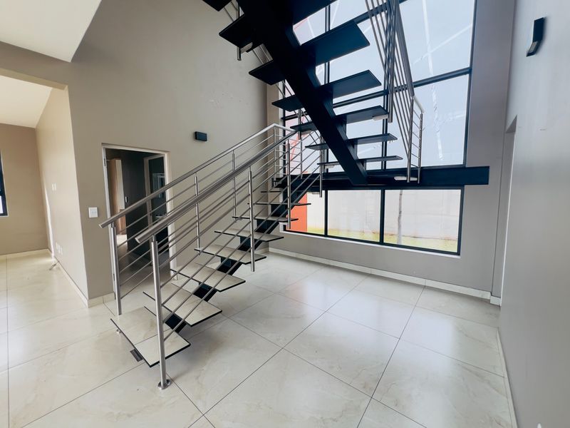 Modern entrance hall featuring a striking floating staircase with stainless steel balustrades, large format floor tiles, and expansive double-volume windows.