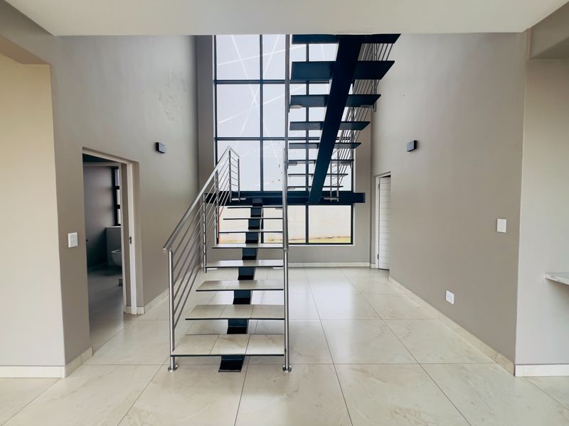 Spacious double-volume entrance hall featuring a modern floating staircase with stainless steel balustrades and large floor-to-ceiling windows.