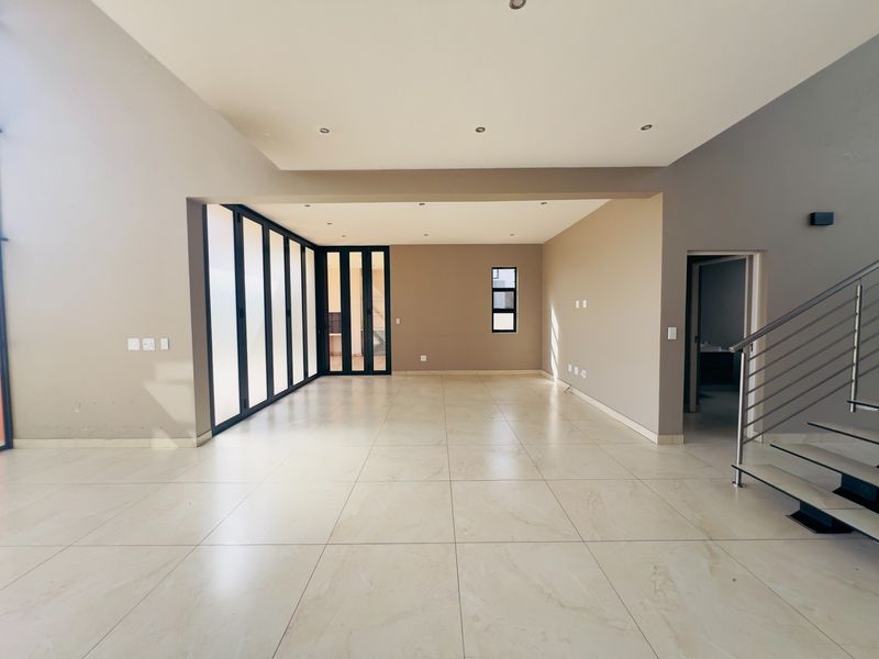 Spacious open-plan living area featuring large format floor tiles, recessed lighting, and modern bi-fold doors leading to the exterior.