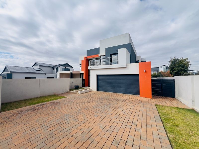Modern double-story residential facade featuring a paved driveway, double garage, and a private balcony with contemporary architectural styling.