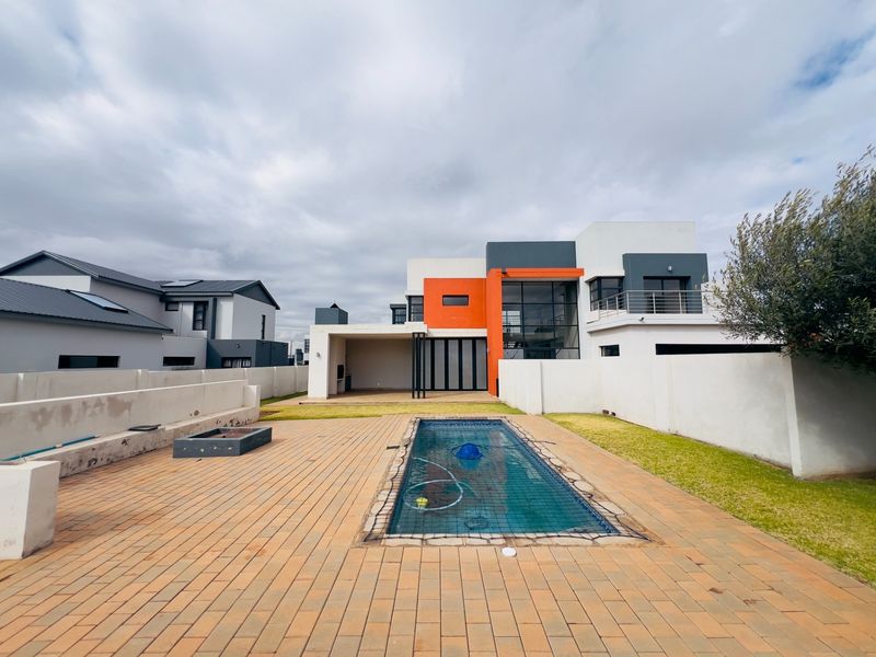 Rear view of a modern two-story house featuring a swimming pool, paved patio area, and a covered outdoor entertainment space.
