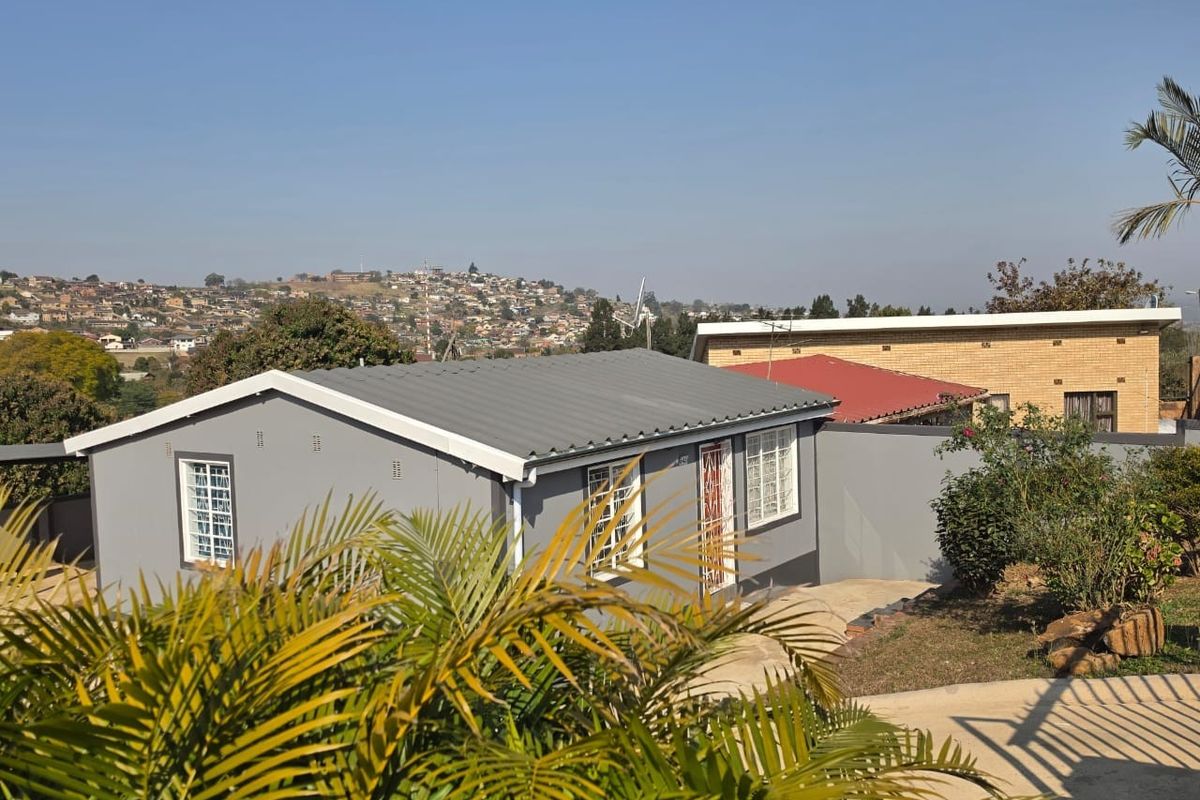 A view of the rear exterior of the house featuring a grey painted facade, corrugated metal roof, and security bars on the windows.