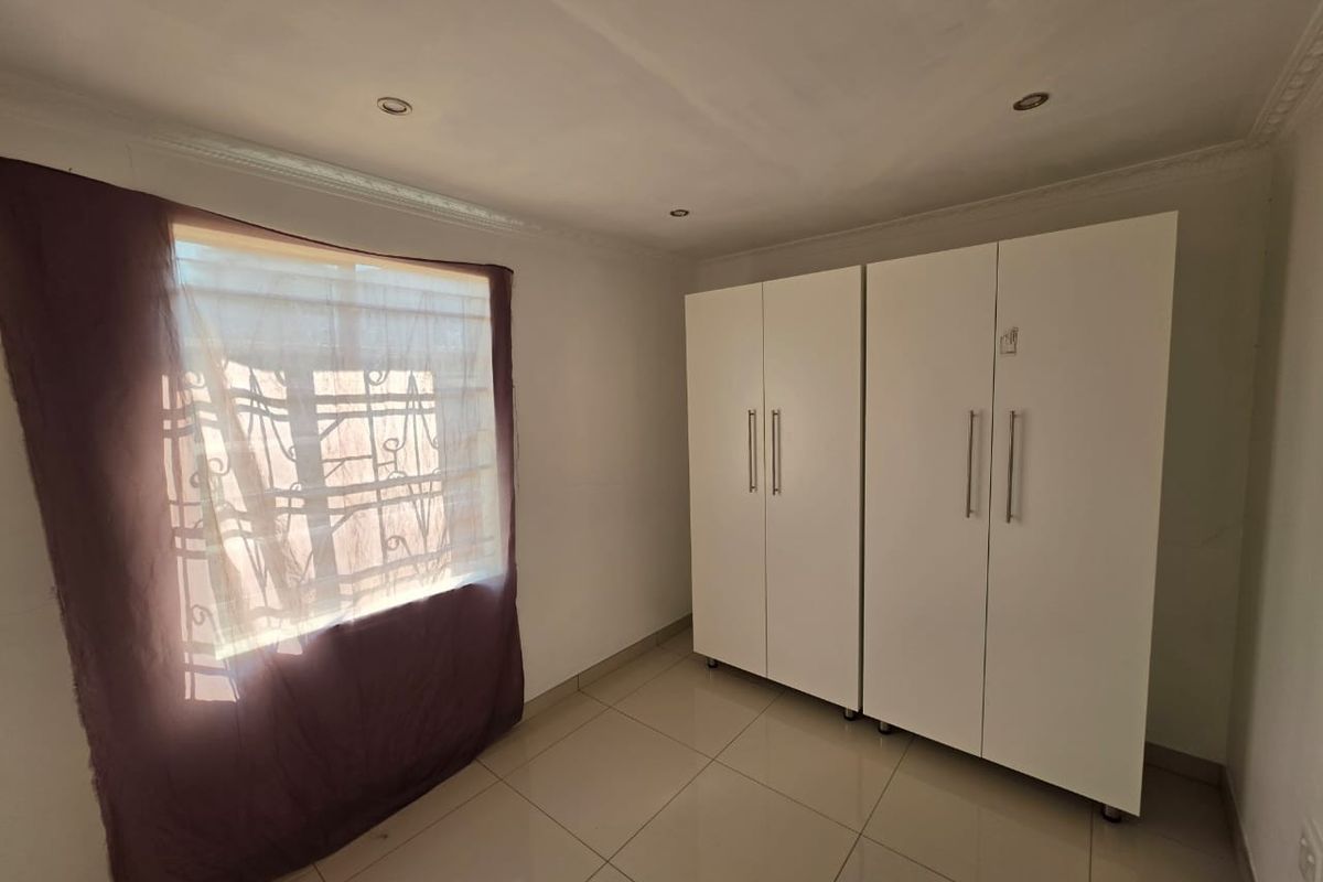 A bright, empty bedroom featuring neutral tiled flooring, recessed downlighting, and white built-in cupboards with modern handles.