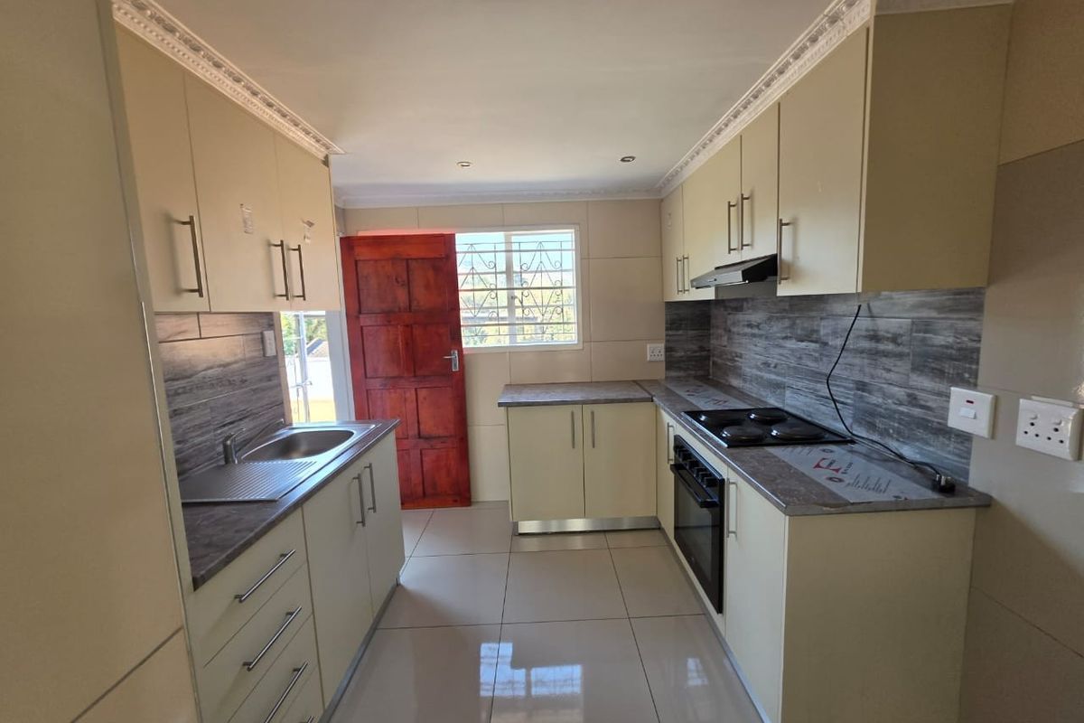A clean, functional kitchen featuring light-toned cabinetry, dark laminate countertops, built-in oven and hob, and tiled finishes throughout.