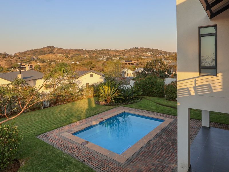 Rear view of the property featuring a swimming pool, brick-paved patio area, and a well-maintained garden with scenic hillside views.