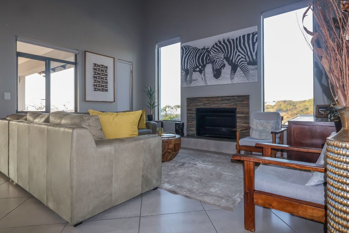 Spacious living room featuring a stone-clad fireplace, large windows providing natural light, and neutral tiled flooring with access to an outdoor area.