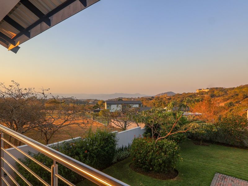 A spacious covered balcony featuring a modern stainless steel balustrade, offering expansive elevated views over the surrounding landscape and garden.