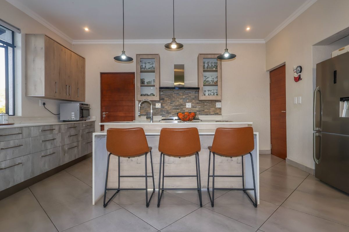 Modern kitchen featuring a central island with breakfast bar seating, stone countertops, built-in cabinetry, and contemporary pendant lighting.