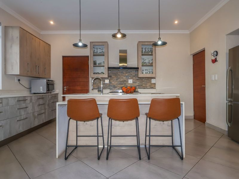 Modern kitchen featuring a central island with breakfast bar seating, stone countertops, built-in cabinetry, and contemporary pendant lighting.