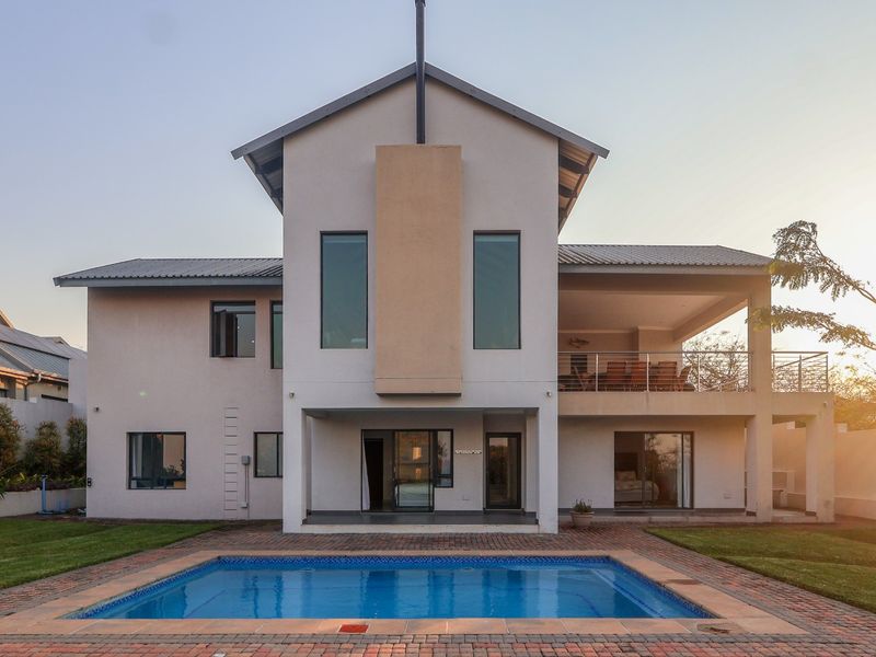 Rear view of a modern two-story house featuring a swimming pool, brick-paved patio area, and an upper-level balcony.