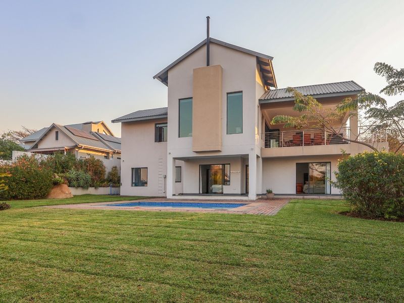 Rear view of a two-story house featuring a swimming pool, landscaped garden, and a covered balcony overlooking the backyard.