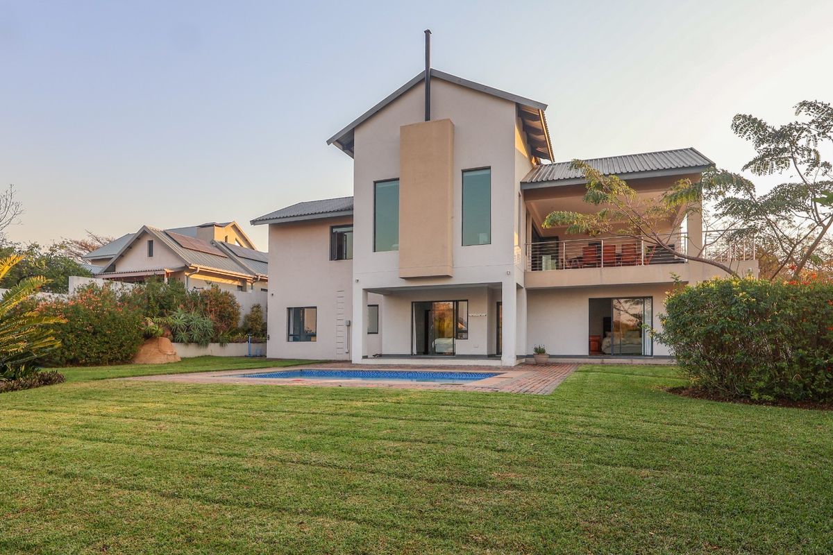 Rear view of a two-story house featuring a swimming pool, landscaped garden, and a covered balcony overlooking the backyard.