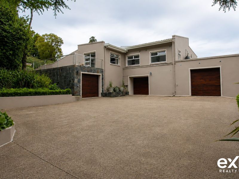 Front elevation of a modern residence featuring a triple garage, stone-clad accents, and a spacious concrete driveway with landscaped retaining walls.