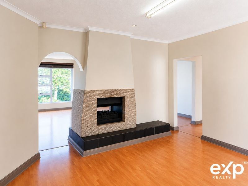 Spacious living room featuring a central built-in fireplace with a tiled hearth, laminate flooring, and an elegant archway leading to an adjacent room.