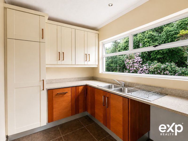 A clean and functional scullery featuring two-tone cabinetry, stone-look countertops, a double stainless steel sink, and a large window overlooking the garden.