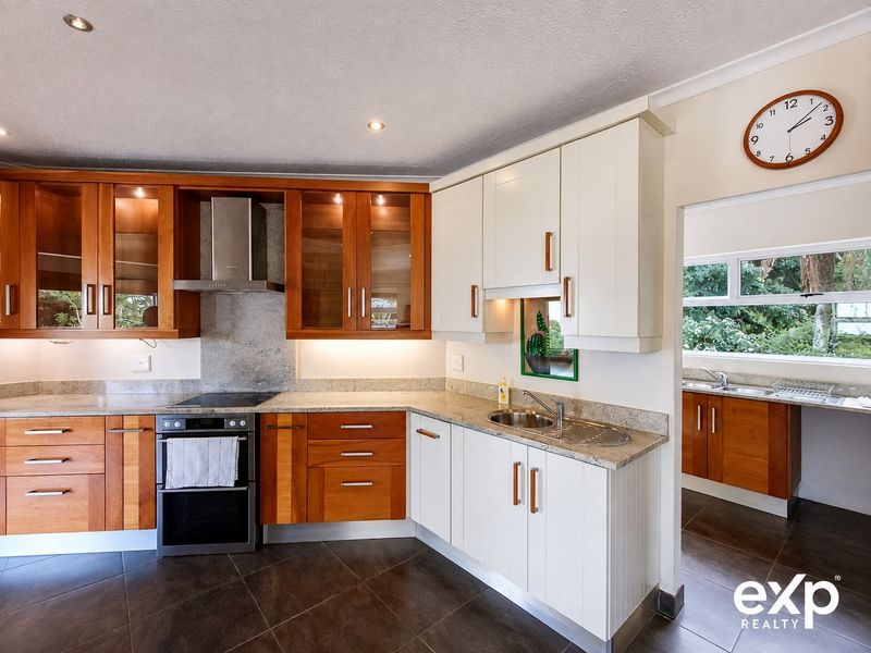 A well-maintained kitchen featuring a mix of wood and white cabinetry, stone countertops, built-in oven, extractor fan, and a connected scullery area.